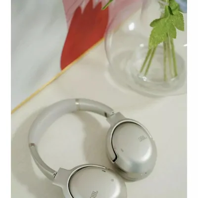 Silver over ear headphones resting flat on a pale table beside a glass vase of green stems