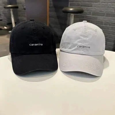 Two baseball caps on stands, one black and one off white, each embroidered with the same small lowercase word