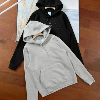 Two complete pullover hoodies, one grey and one black, laid together on a wooden floor with their hoods and kangaroo pockets visible