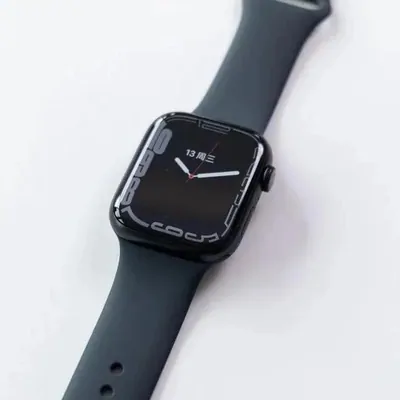 A black square cased smartwatch with a dark grey sport band, lying face up on a white surface