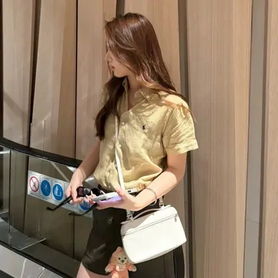 A woman on an escalator in a yellow short sleeved polo shirt, a small white shoulder bag at her hip